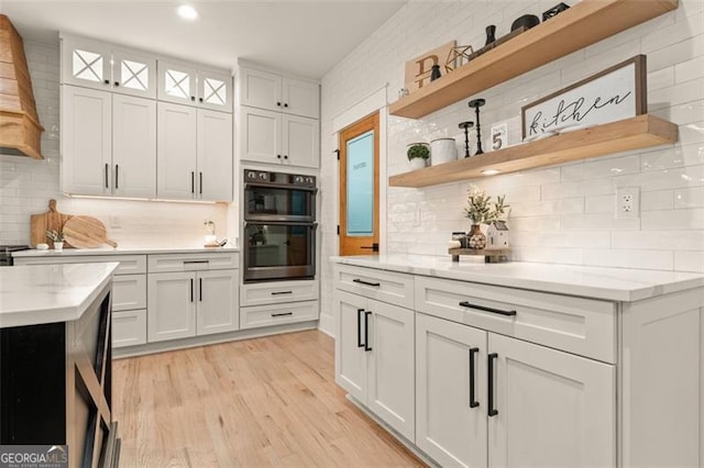 kitchen with light hardwood / wood-style floors, tasteful backsplash, stainless steel double oven, and white cabinets