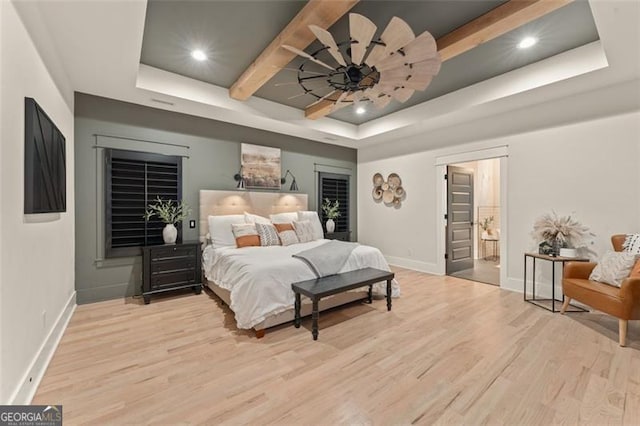 bedroom featuring ceiling fan, ensuite bathroom, light hardwood / wood-style floors, and a raised ceiling