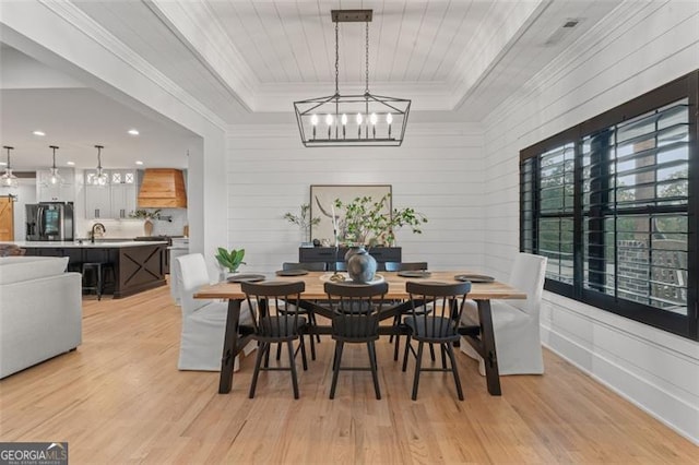 dining space with an inviting chandelier, a tray ceiling, and light wood-type flooring