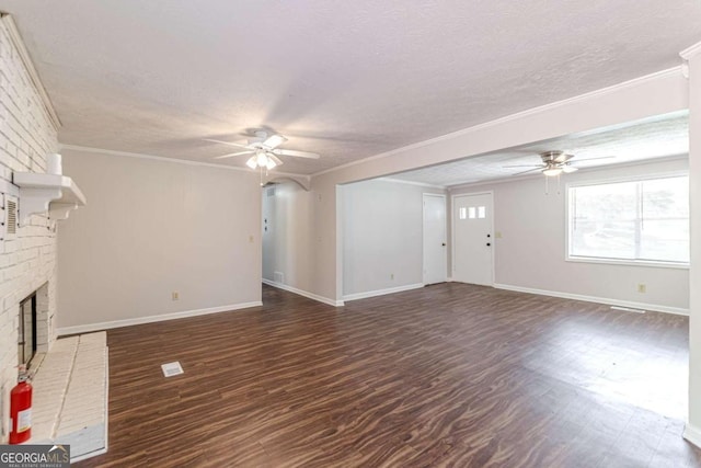 unfurnished living room with ceiling fan, a textured ceiling, a brick fireplace, ornamental molding, and dark wood-type flooring