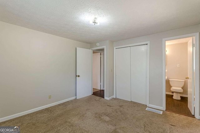 unfurnished bedroom featuring a closet, a textured ceiling, ensuite bath, and light colored carpet