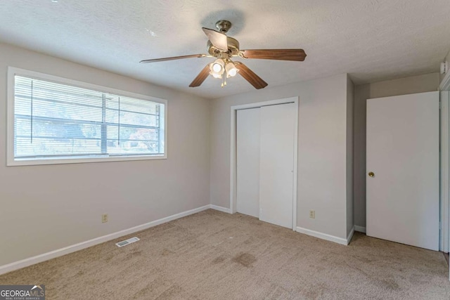 unfurnished bedroom with ceiling fan, light carpet, and a textured ceiling