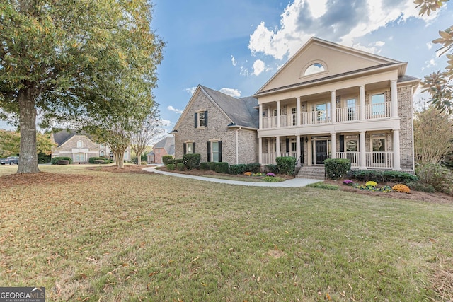 greek revival house with covered porch, a front yard, and a balcony