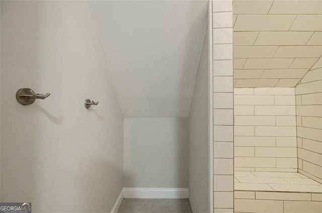 bathroom with a tile shower and lofted ceiling