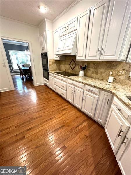 kitchen featuring hardwood / wood-style floors, black appliances, white cabinetry, and custom range hood