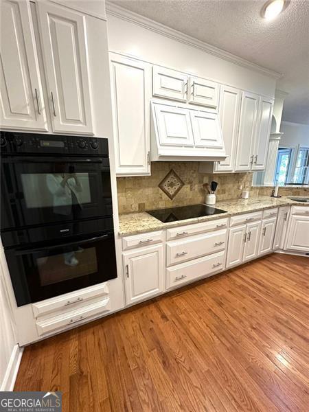 kitchen with black appliances, decorative backsplash, white cabinetry, and light hardwood / wood-style flooring