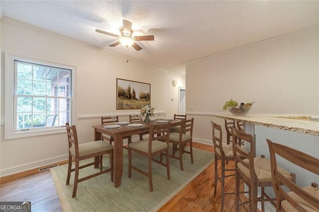 dining room featuring crown molding, hardwood / wood-style floors, ceiling fan, and a textured ceiling