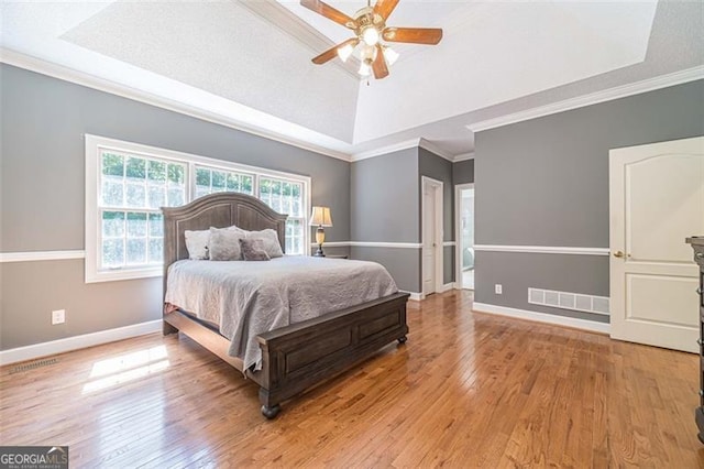 bedroom featuring light wood-type flooring, a raised ceiling, ceiling fan, and crown molding