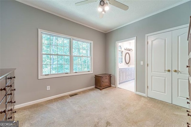 unfurnished bedroom with ensuite bathroom, ornamental molding, a textured ceiling, light colored carpet, and ceiling fan