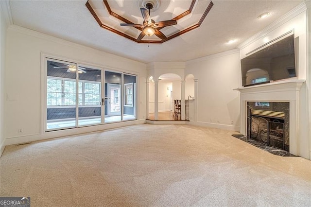 unfurnished living room featuring crown molding, ceiling fan, ornate columns, a fireplace, and light colored carpet