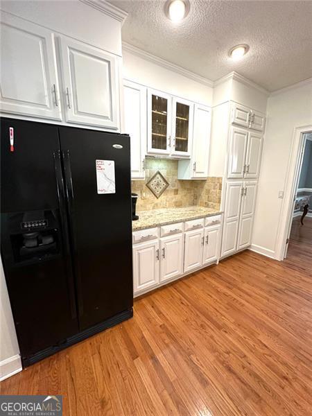 kitchen with decorative backsplash, black fridge with ice dispenser, white cabinetry, and light hardwood / wood-style flooring