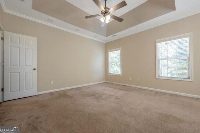 carpeted spare room with crown molding, a healthy amount of sunlight, ceiling fan, and a raised ceiling