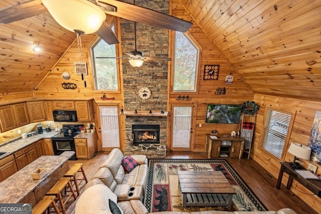 living room featuring a stone fireplace, hardwood / wood-style floors, wooden walls, high vaulted ceiling, and wooden ceiling