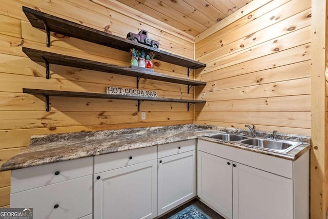 kitchen featuring wooden walls, sink, dark stone countertops, white cabinets, and wood ceiling