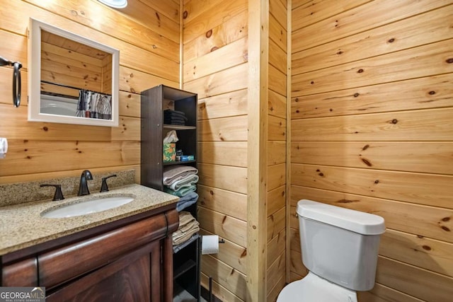 bathroom with vanity, wooden walls, and toilet