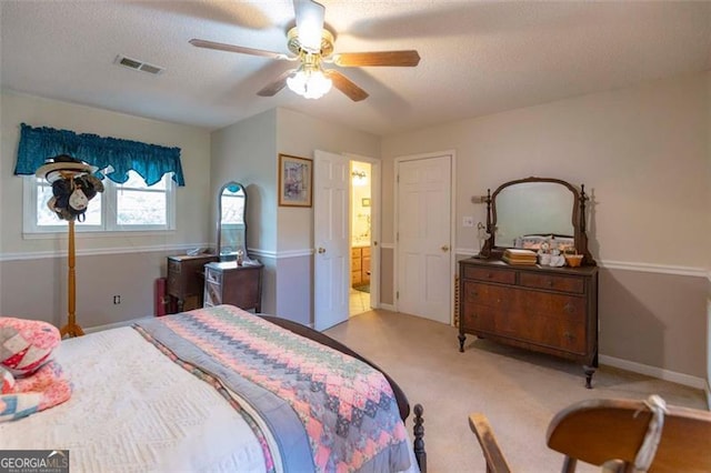 bedroom with a textured ceiling, light colored carpet, ceiling fan, and ensuite bath