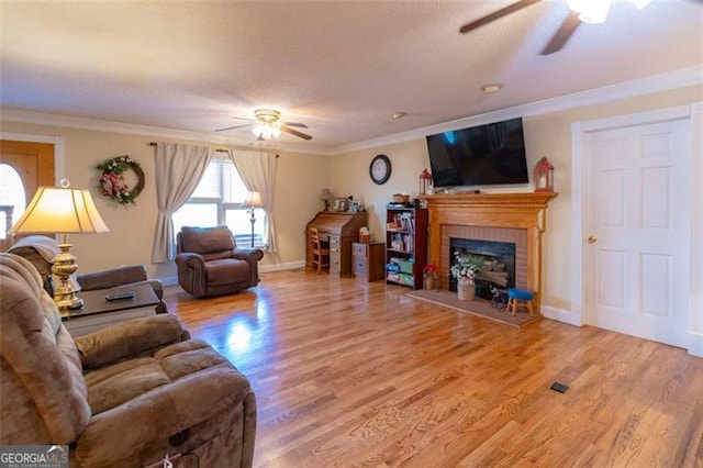 living room featuring a textured ceiling, hardwood / wood-style flooring, ceiling fan, crown molding, and a fireplace