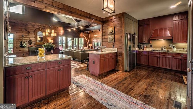 kitchen with a kitchen island, appliances with stainless steel finishes, dark hardwood / wood-style floors, decorative light fixtures, and light stone counters