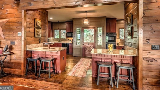 kitchen with dark hardwood / wood-style flooring, a kitchen island, a kitchen bar, black appliances, and decorative light fixtures