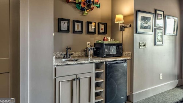 bar with light stone countertops, black appliances, and sink