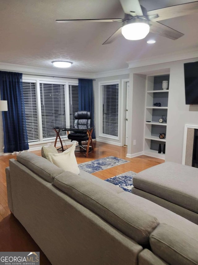 living room with a textured ceiling, ceiling fan, crown molding, hardwood / wood-style flooring, and built in shelves