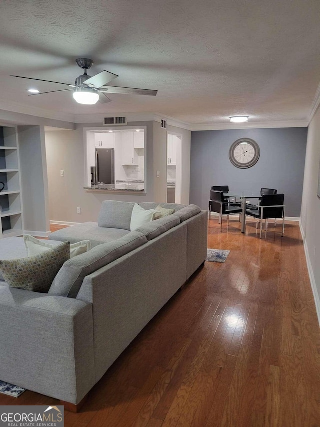 living room featuring ceiling fan, a textured ceiling, wood-type flooring, and ornamental molding