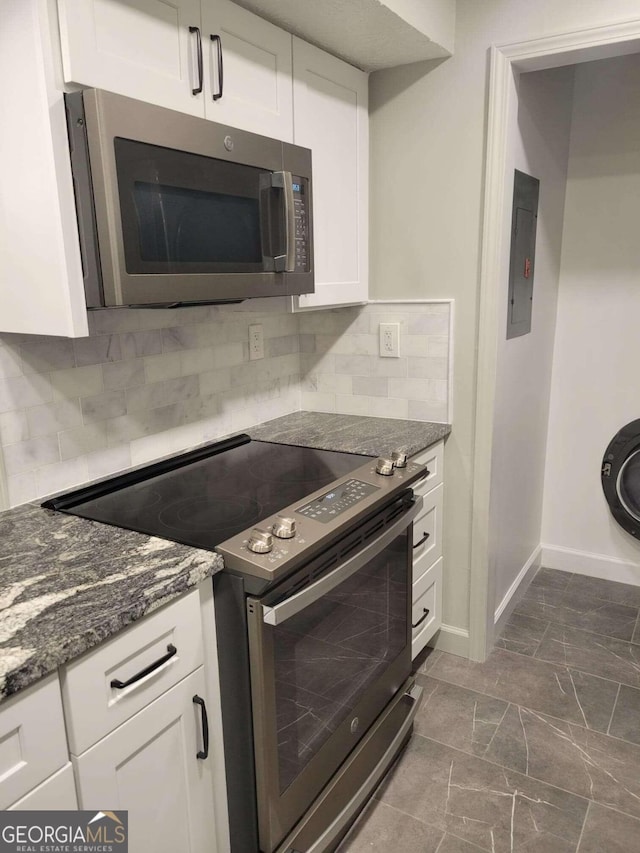 kitchen with decorative backsplash, dark stone countertops, white cabinets, electric panel, and appliances with stainless steel finishes