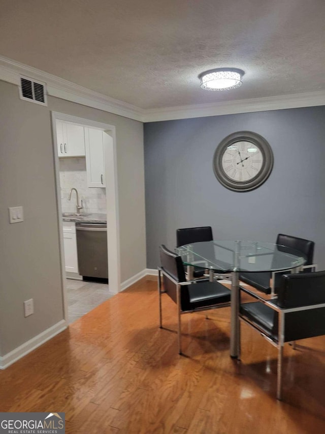 dining area with light hardwood / wood-style floors, crown molding, a textured ceiling, and sink