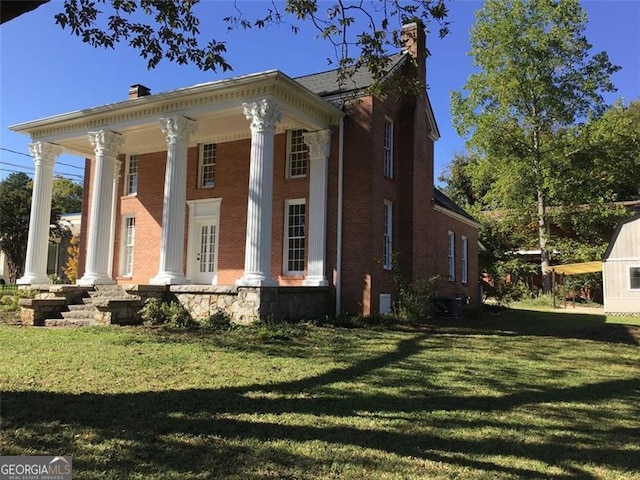 view of front facade featuring brick siding, covered porch, a front yard, and a chimney