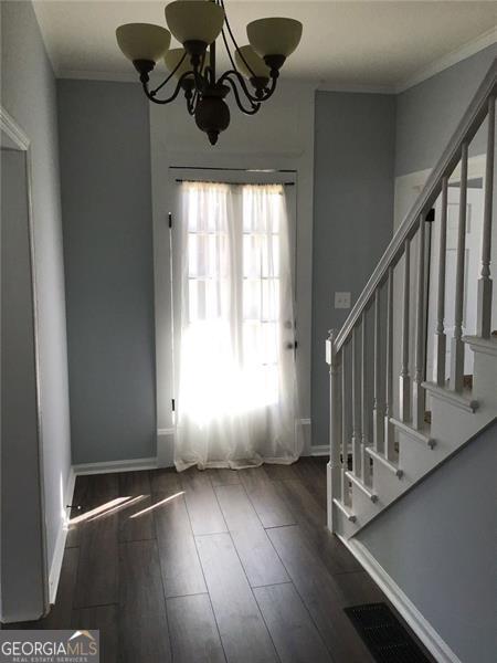foyer entrance featuring wood finished floors, stairway, baseboards, a chandelier, and ornamental molding