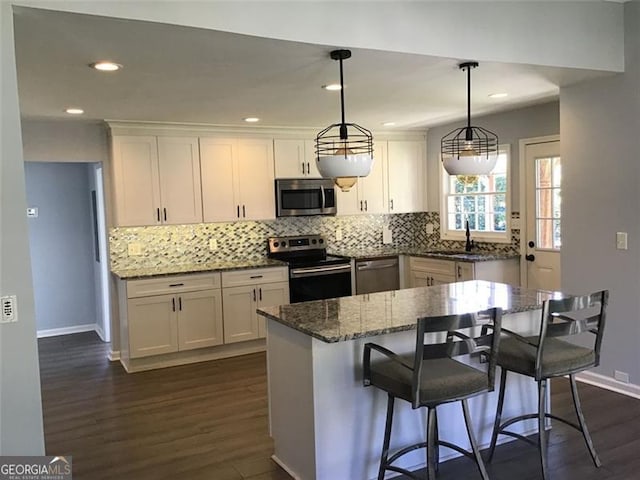 kitchen with dark stone countertops, stainless steel appliances, pendant lighting, and white cabinets