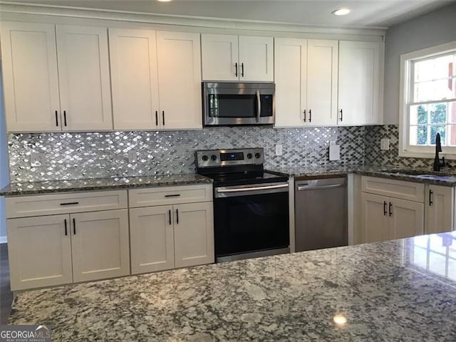 kitchen featuring appliances with stainless steel finishes, a sink, dark stone countertops, white cabinetry, and backsplash