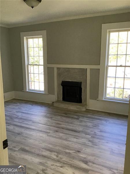 unfurnished living room with ornamental molding, wood finished floors, a fireplace with raised hearth, and baseboards