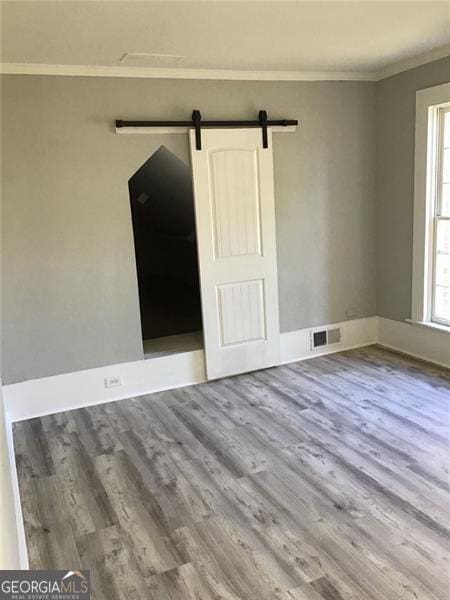 unfurnished room featuring wood finished floors, crown molding, a barn door, and baseboards