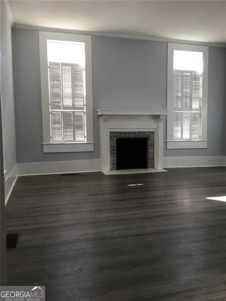 unfurnished living room with wood finished floors, baseboards, plenty of natural light, a fireplace with flush hearth, and ornamental molding