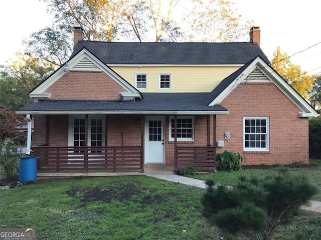 view of front facade featuring a chimney, brick siding, covered porch, and a front lawn