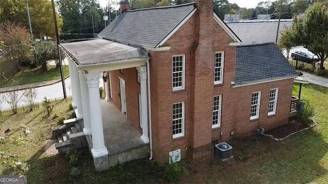 view of home's exterior featuring a chimney, brick siding, central AC unit, and a shingled roof
