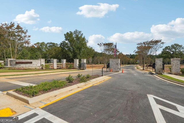 view of road featuring a gated entry, curbs, and sidewalks