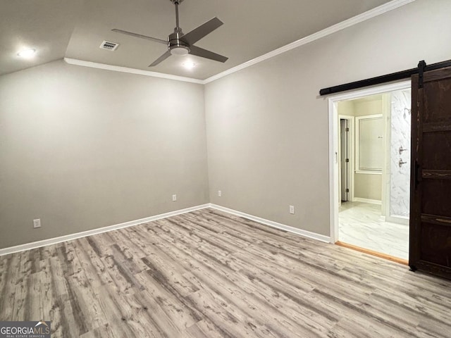 spare room featuring ceiling fan, a barn door, light hardwood / wood-style flooring, crown molding, and vaulted ceiling