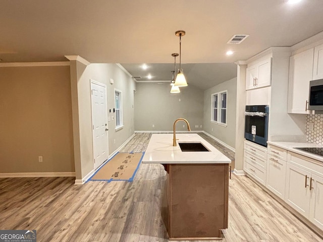 kitchen featuring stainless steel oven, light hardwood / wood-style flooring, decorative light fixtures, a kitchen island with sink, and white cabinets