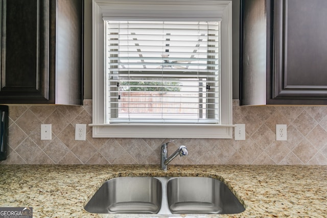 kitchen featuring dark brown cabinets, tasteful backsplash, light stone countertops, and sink