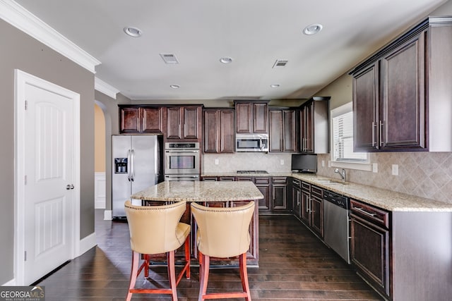 kitchen featuring stainless steel appliances, ornamental molding, a center island, dark hardwood / wood-style flooring, and tasteful backsplash