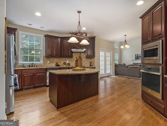 kitchen with decorative light fixtures, stainless steel appliances, and light hardwood / wood-style flooring