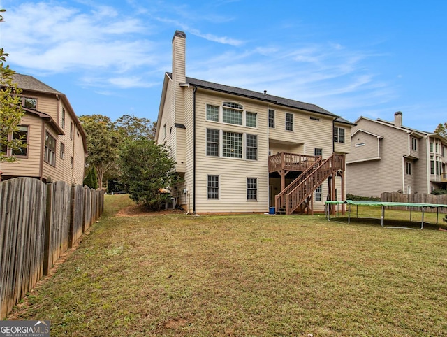 rear view of property with a lawn, a trampoline, and a deck