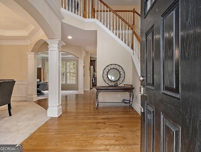 entryway featuring decorative columns, crown molding, a high ceiling, and light wood-type flooring