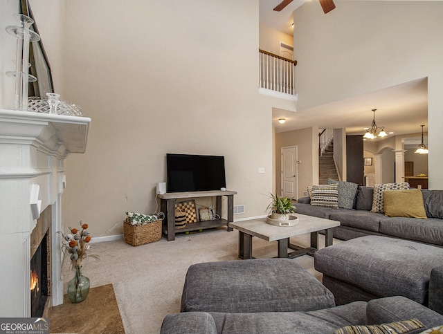 carpeted living room with a towering ceiling, ceiling fan with notable chandelier, and a tiled fireplace