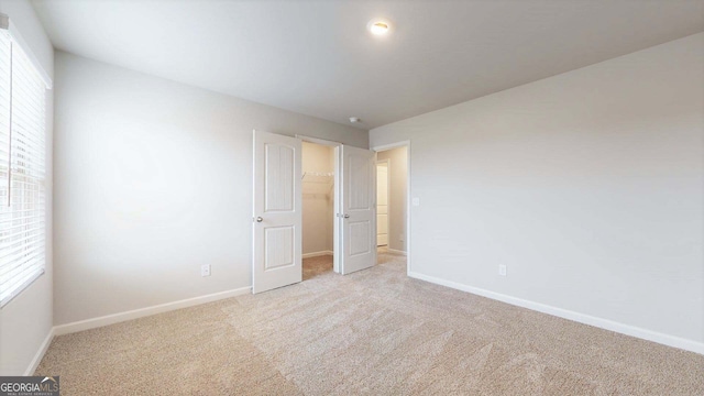 unfurnished bedroom featuring light colored carpet, a spacious closet, and multiple windows