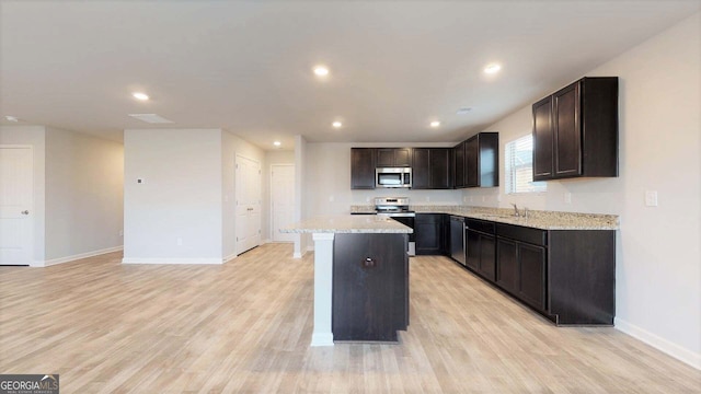 kitchen with sink, light stone countertops, light wood-type flooring, a kitchen island, and stainless steel appliances