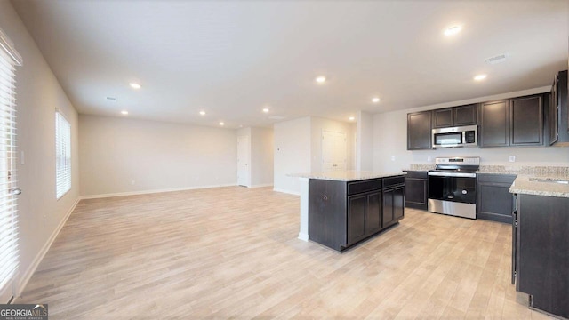 kitchen featuring sink, light hardwood / wood-style flooring, appliances with stainless steel finishes, a kitchen island, and light stone counters