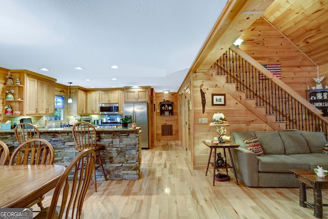 kitchen with light hardwood / wood-style flooring, kitchen peninsula, decorative light fixtures, wooden walls, and appliances with stainless steel finishes